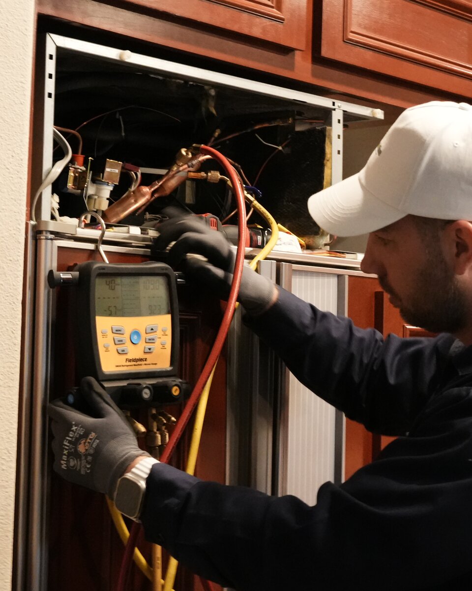 Peter, senior Sub-Zero specialist, running a refrigerant manifold diagnostic on an open built-in Sub-Zero sealed system in a Bay Area cherry-cabinet kitchen