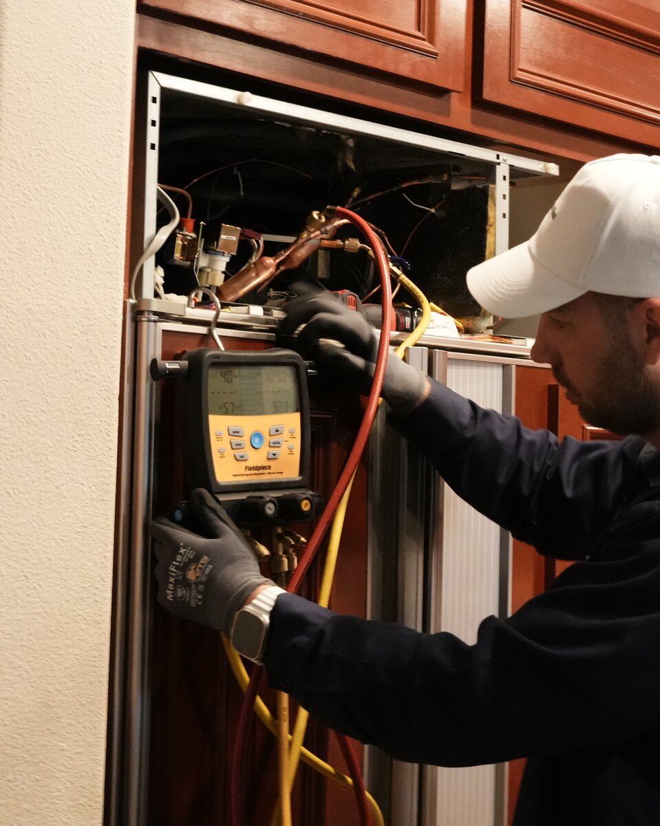 Sergei, senior Sub-Zero specialist, running a refrigerant manifold diagnostic on an open built-in Sub-Zero sealed system in a Bay Area cherry-cabinet kitchen